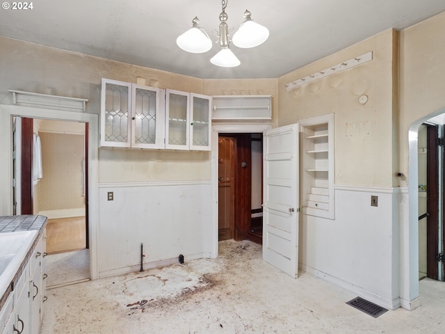 kitchen with tile counters, hanging light fixtures, an inviting chandelier, and white cabinetry