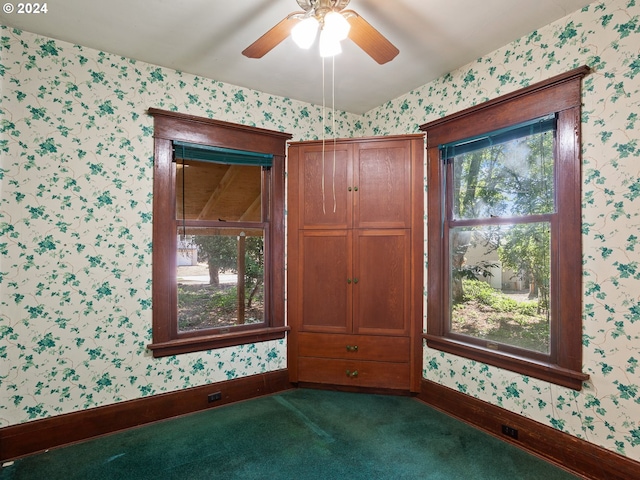 empty room featuring ceiling fan and dark colored carpet