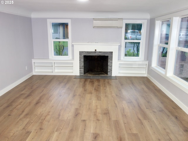 unfurnished living room with a wall mounted AC, a stone fireplace, and light hardwood / wood-style flooring