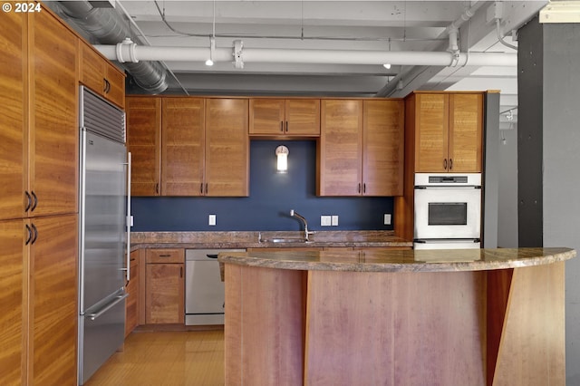 kitchen with dark stone counters, stainless steel appliances, light hardwood / wood-style floors, decorative light fixtures, and sink