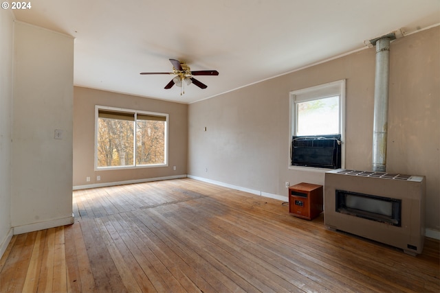 unfurnished living room with heating unit, ceiling fan, a healthy amount of sunlight, and light wood-type flooring