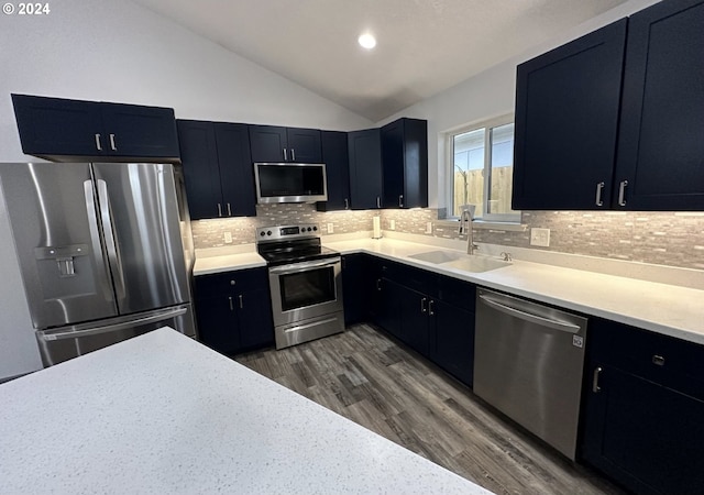 kitchen featuring stainless steel appliances, vaulted ceiling, a sink, and dark cabinets