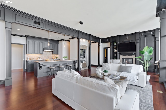 living room featuring crown molding, decorative columns, and dark wood-type flooring