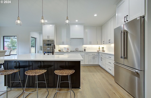 kitchen with light wood-style floors, white cabinets, a sink, and high end refrigerator