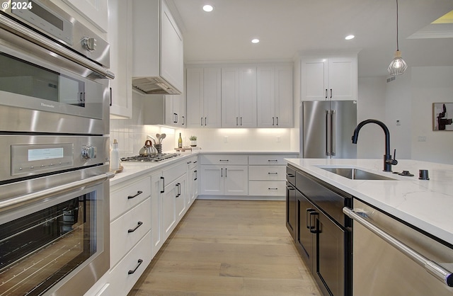 kitchen with light wood finished floors, stainless steel appliances, decorative backsplash, white cabinets, and a sink