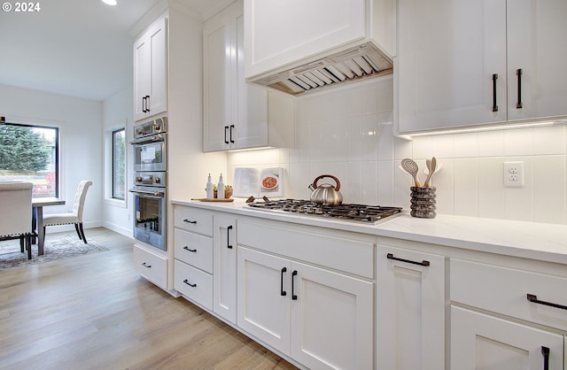 kitchen with stainless steel appliances, baseboards, white cabinets, light wood-type flooring, and decorative backsplash