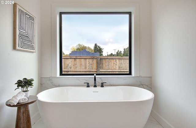 bathroom featuring marble finish floor, baseboards, and a soaking tub