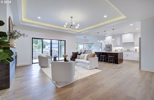 living room featuring a tray ceiling, light wood-style flooring, and an inviting chandelier