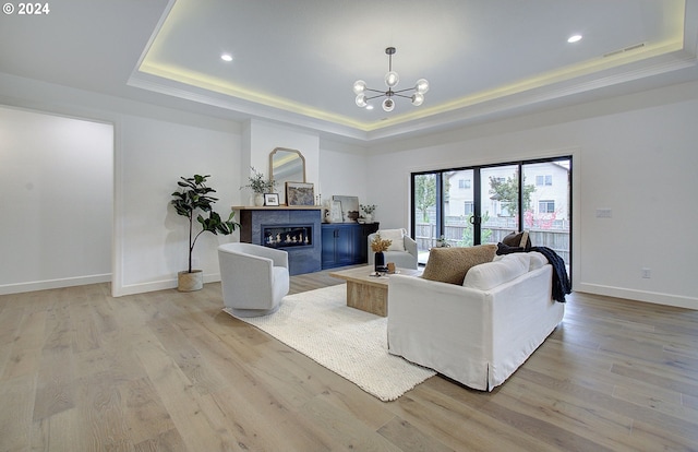 living room featuring light wood finished floors, a glass covered fireplace, a raised ceiling, and baseboards