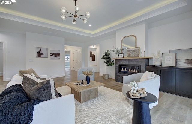 living room with a high end fireplace, light wood-type flooring, and a tray ceiling