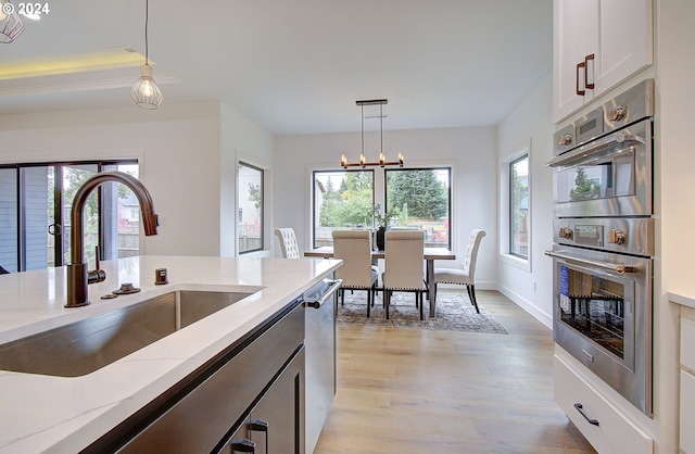 kitchen with light wood-style flooring, light stone counters, decorative light fixtures, stainless steel appliances, and a sink