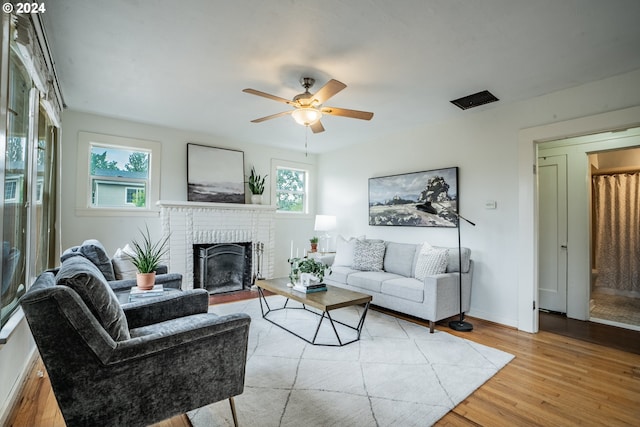 living room with light hardwood / wood-style floors, a brick fireplace, ceiling fan, and a wealth of natural light