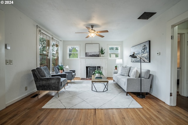 living room with ceiling fan, light hardwood / wood-style floors, and a brick fireplace