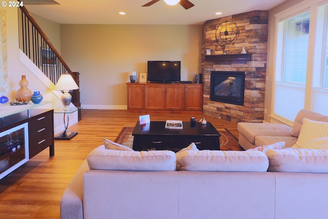 living room with a stone fireplace, light wood-type flooring, and ceiling fan