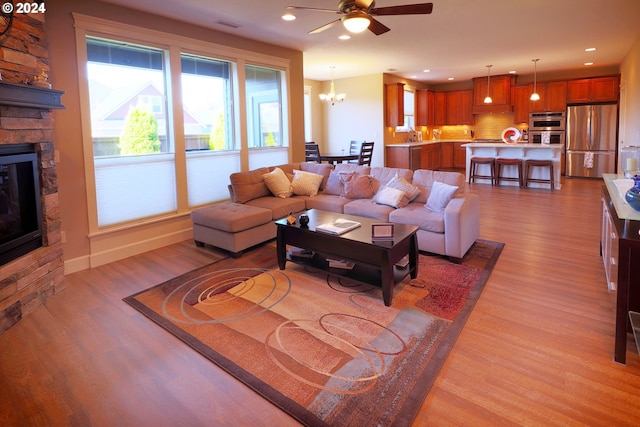 living room with a fireplace, light hardwood / wood-style floors, and ceiling fan with notable chandelier