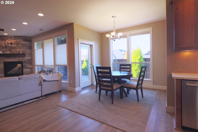 dining area featuring dark wood-type flooring, a chandelier, and a stone fireplace