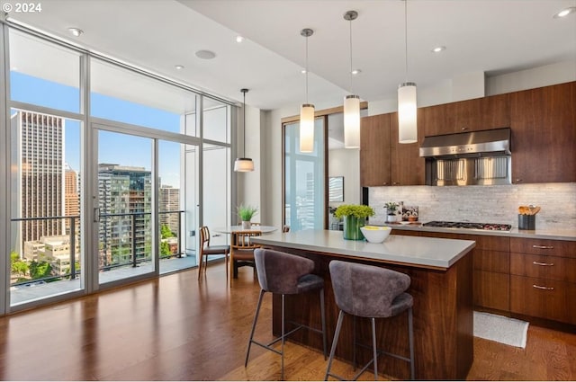 kitchen with dark wood-type flooring, a center island, decorative light fixtures, a wall of windows, and ventilation hood