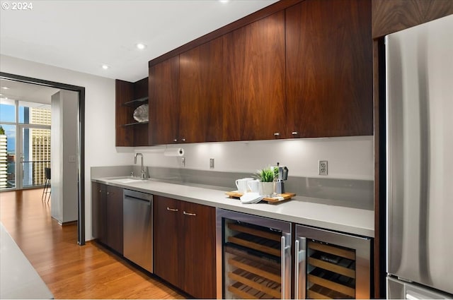 kitchen with stainless steel appliances, beverage cooler, sink, and light hardwood / wood-style flooring