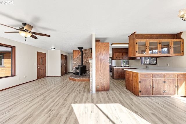 kitchen with ceiling fan, light hardwood / wood-style flooring, sink, and a wood stove