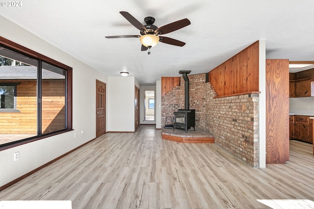 unfurnished living room featuring ceiling fan, a wood stove, brick wall, a textured ceiling, and light wood-type flooring