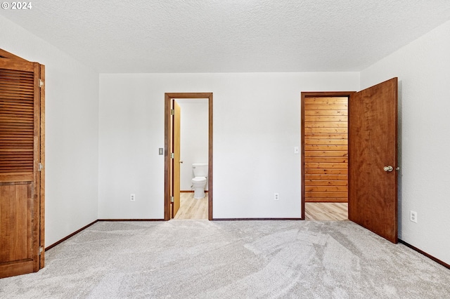 unfurnished bedroom with a closet, light colored carpet, ensuite bathroom, and a textured ceiling