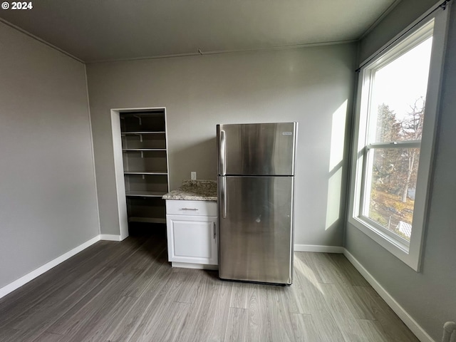 kitchen with light stone countertops, hardwood / wood-style flooring, stainless steel refrigerator, and white cabinetry