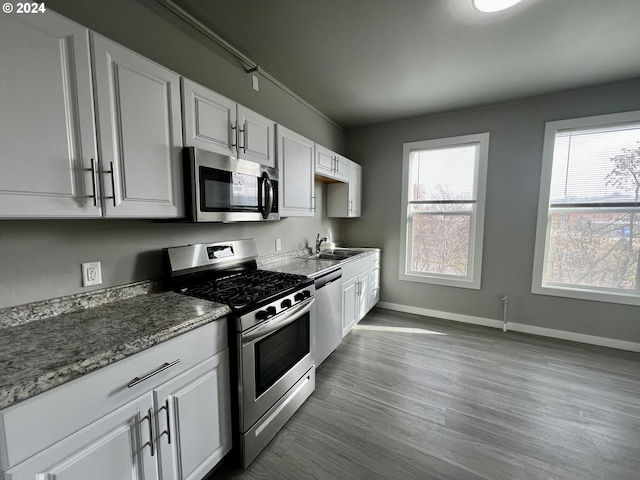 kitchen featuring stainless steel appliances, sink, wood-type flooring, dark stone countertops, and white cabinets