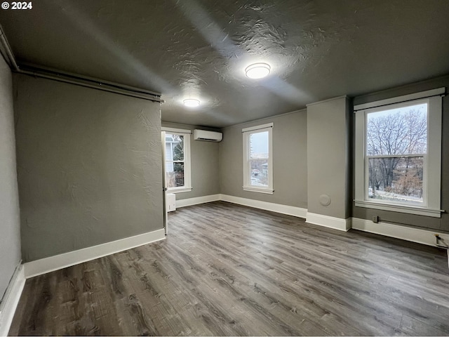 additional living space featuring wood-type flooring, a textured ceiling, a wall unit AC, and a healthy amount of sunlight