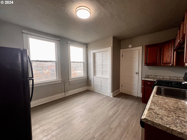 kitchen featuring black refrigerator, a textured ceiling, light wood-type flooring, and sink