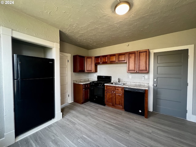 kitchen with a textured ceiling, sink, light hardwood / wood-style flooring, and black appliances