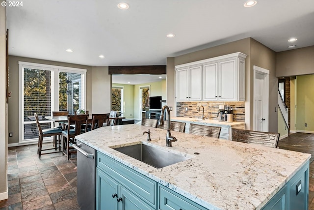 kitchen featuring white cabinetry, a center island with sink, decorative backsplash, blue cabinetry, and sink