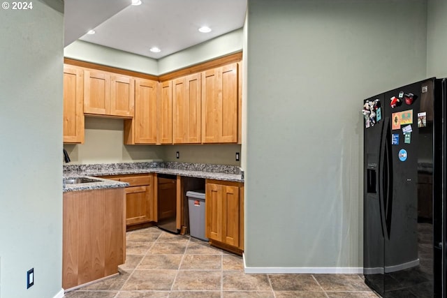 kitchen with sink, light stone counters, and black fridge