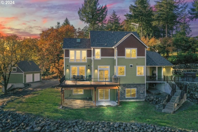 back house at dusk with a garage, an outbuilding, and a lawn