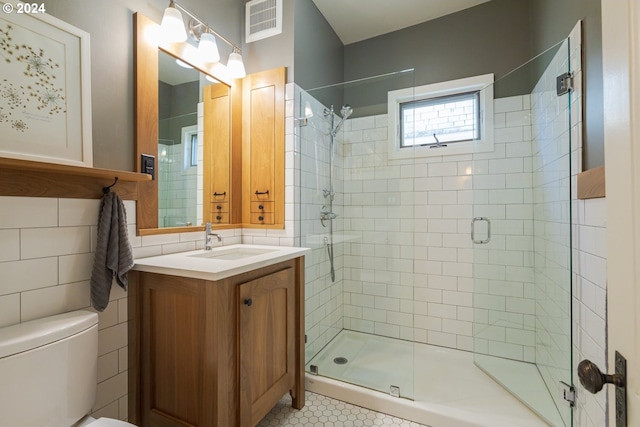 bathroom featuring vanity, a shower with shower door, tile patterned flooring, tile walls, and toilet