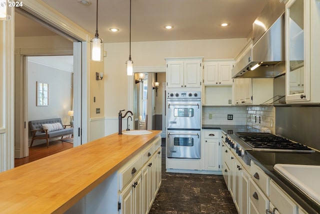 kitchen featuring decorative light fixtures, stainless steel appliances, white cabinetry, wall chimney exhaust hood, and wooden counters