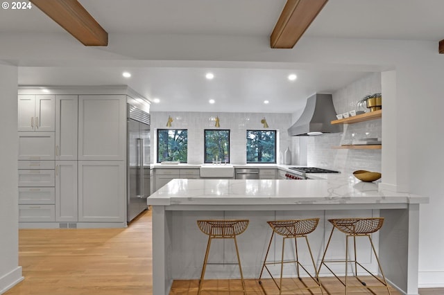 kitchen with decorative backsplash, wall chimney exhaust hood, a kitchen breakfast bar, kitchen peninsula, and light hardwood / wood-style floors