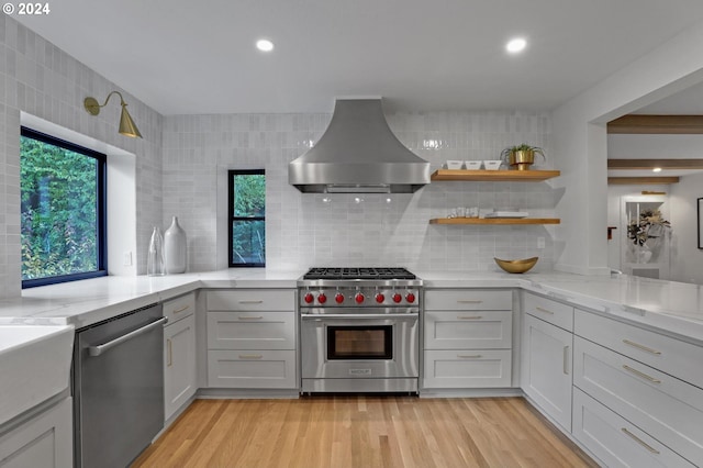 kitchen featuring light stone countertops, wall chimney range hood, stainless steel appliances, and light wood-type flooring