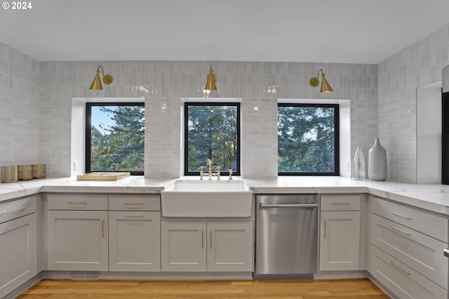 kitchen with sink, light wood-type flooring, dishwasher, tile walls, and light stone counters