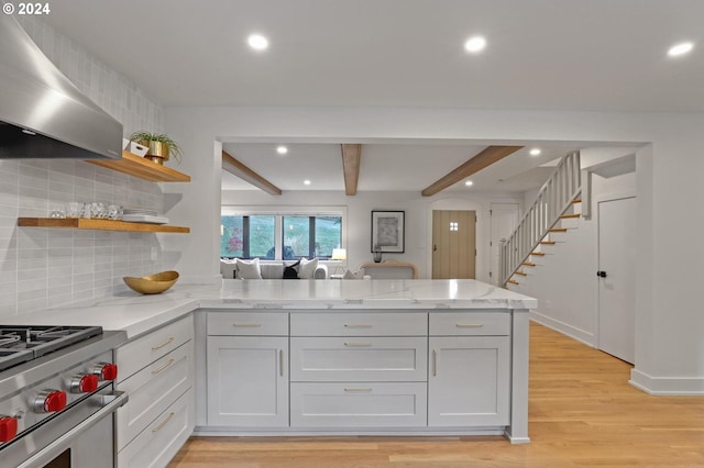 kitchen with light stone countertops, high end stainless steel range, wall chimney exhaust hood, decorative backsplash, and light hardwood / wood-style flooring