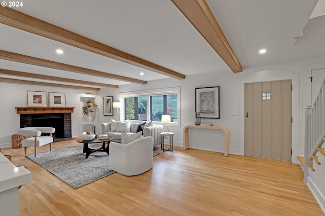 living room with a fireplace, beam ceiling, and light wood-type flooring