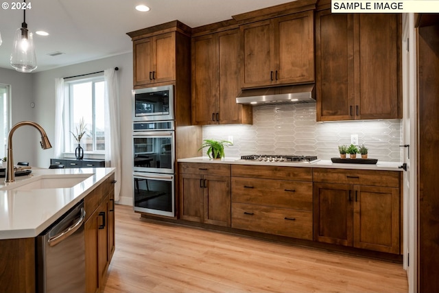 kitchen with light wood-type flooring, tasteful backsplash, stainless steel appliances, sink, and decorative light fixtures