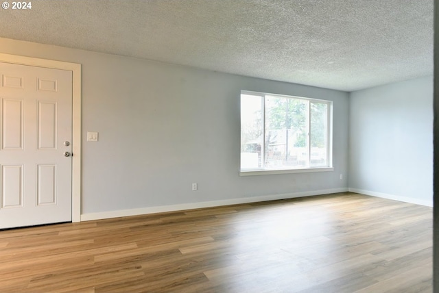 empty room with a textured ceiling and light hardwood / wood-style flooring