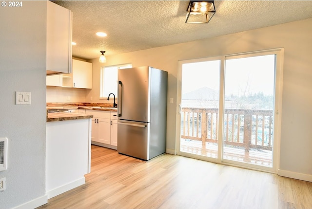 kitchen with light hardwood / wood-style floors, white cabinets, stainless steel refrigerator, wooden counters, and sink