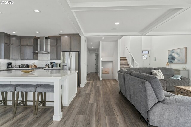 kitchen featuring a large island, wall chimney range hood, a breakfast bar, dark hardwood / wood-style floors, and dark brown cabinetry