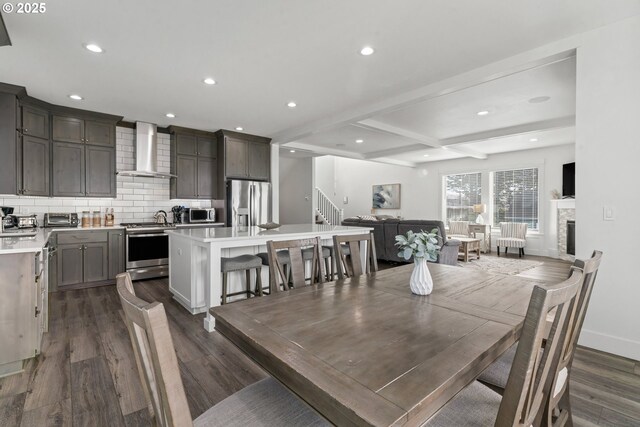 dining space with beamed ceiling, coffered ceiling, a stone fireplace, and dark hardwood / wood-style floors