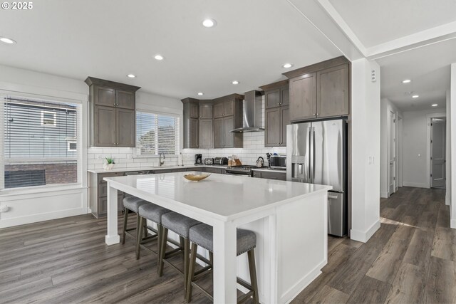 kitchen featuring stainless steel appliances, a kitchen breakfast bar, a kitchen island, decorative backsplash, and wall chimney exhaust hood