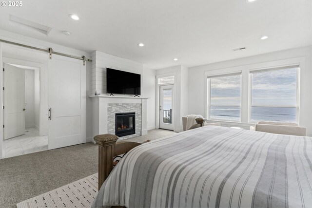 bedroom featuring a barn door, light carpet, and a stone fireplace