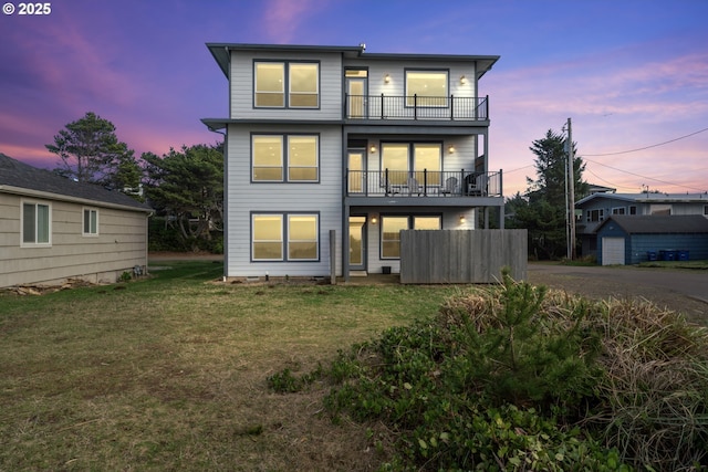 back house at dusk with a balcony and a lawn