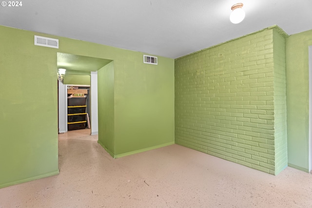 spare room featuring brick wall, visible vents, and baseboards