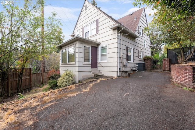 view of front of home with entry steps, cooling unit, a shingled roof, fence, and driveway